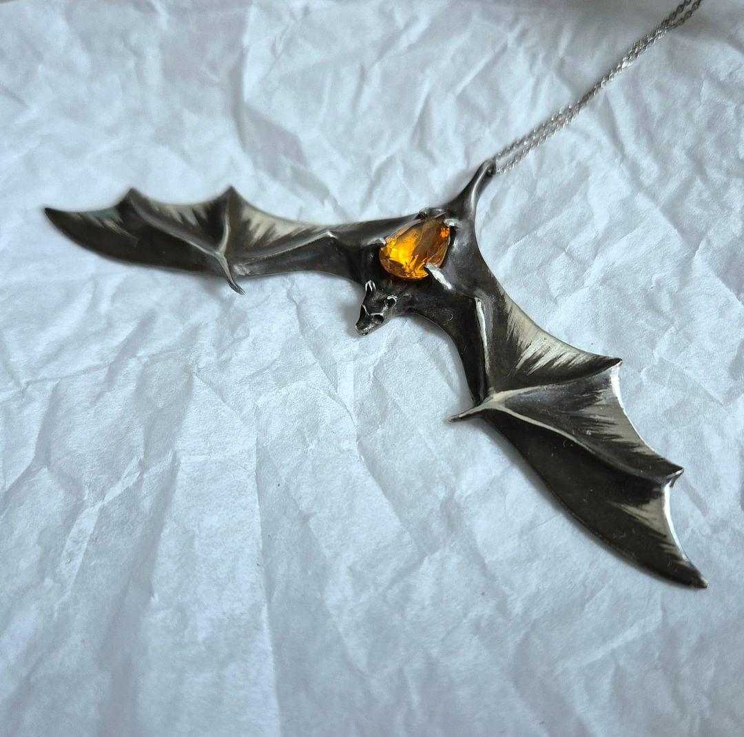 Silver Bat necklace with citrine gemstone displayed on soft textured fabric