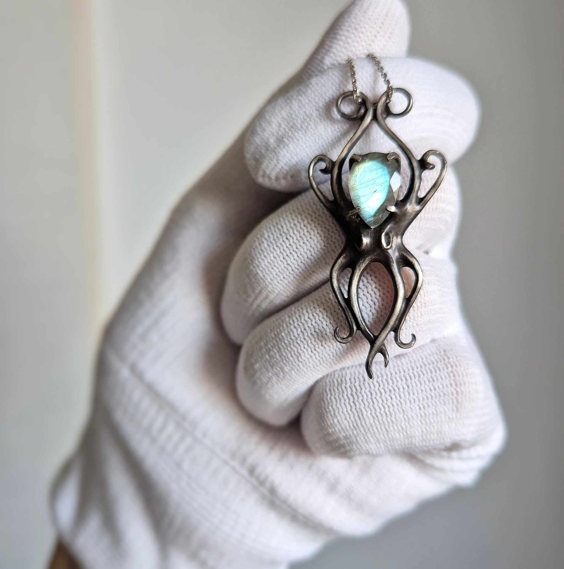 Silver Octopus necklace held in a gloved hand, showing the faceted cyan labradorite