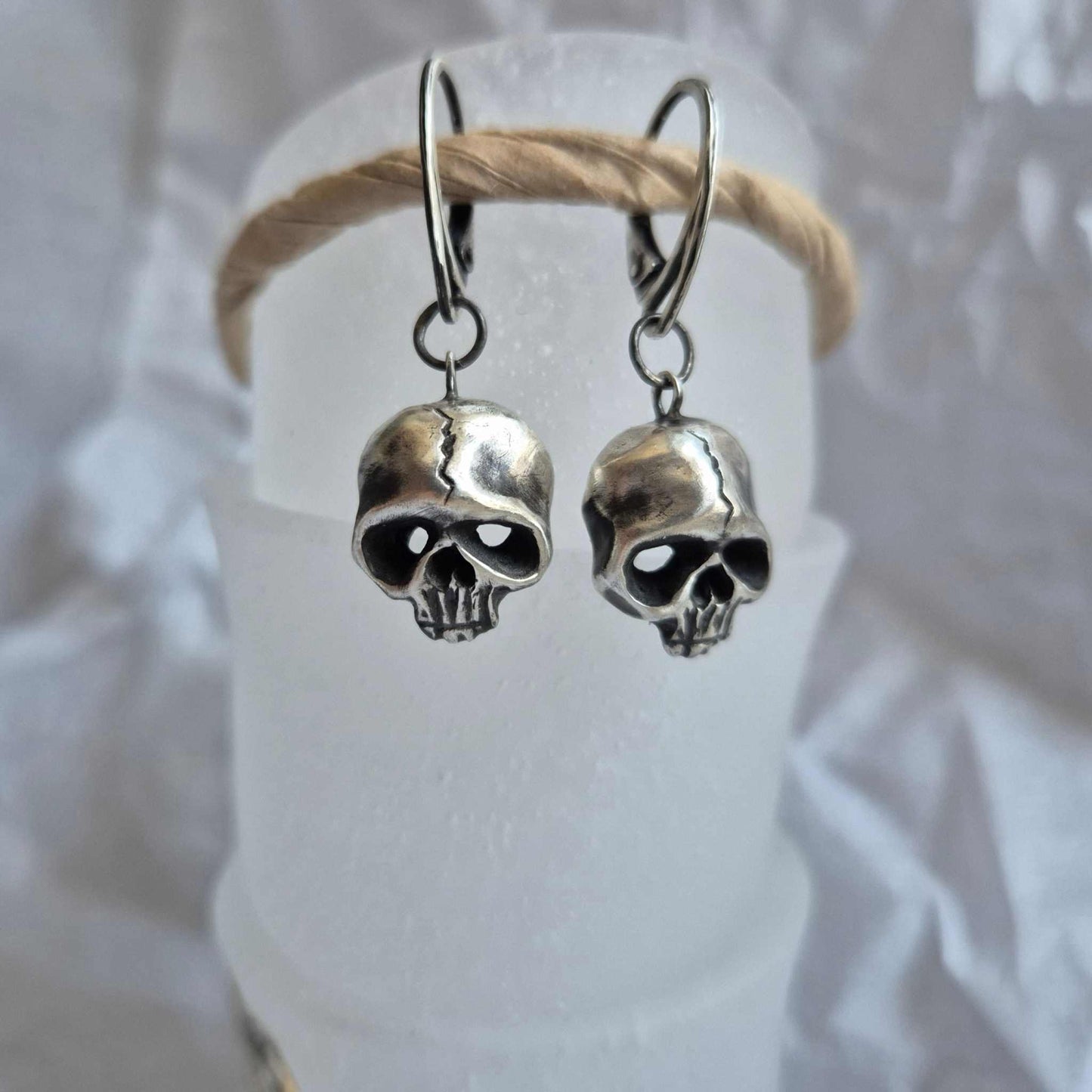 Silver Skull earrings dangling on white display