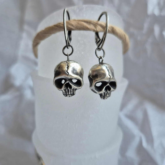 Silver Skull earrings dangling on white display