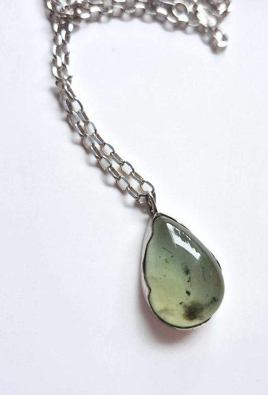 Close-up of prehnite pendant with silver chain loosely coiled