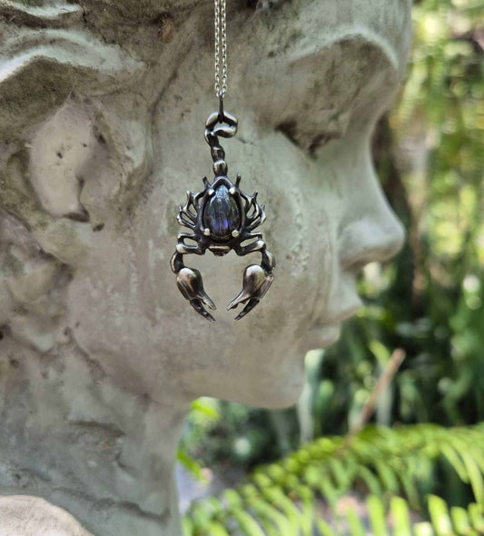 Handmade Scorpion pendant with purple labradorite, shown outdoors in natural light with a girl sculpture as a background
