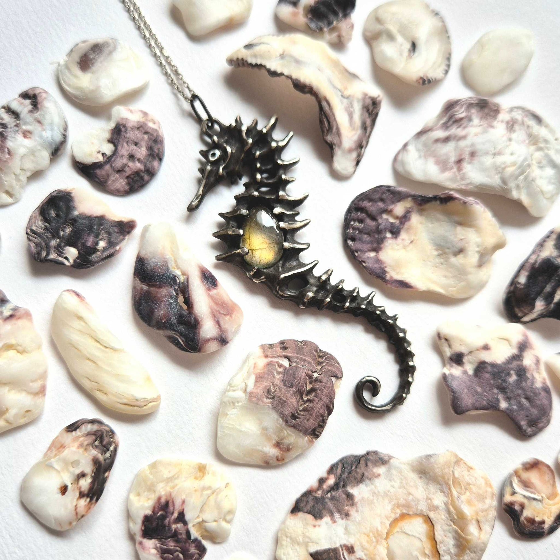 Handmade silver Seahorse necklace with labradorite gemstone resting on a white surface with seashells around.