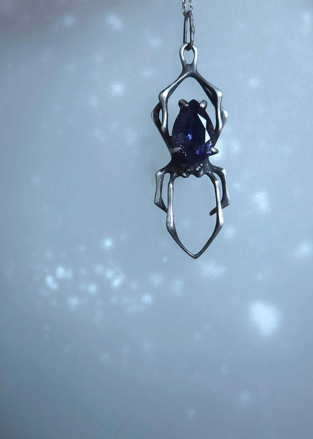 Silver spider pendant with iolite sunstone, photographed on textured background