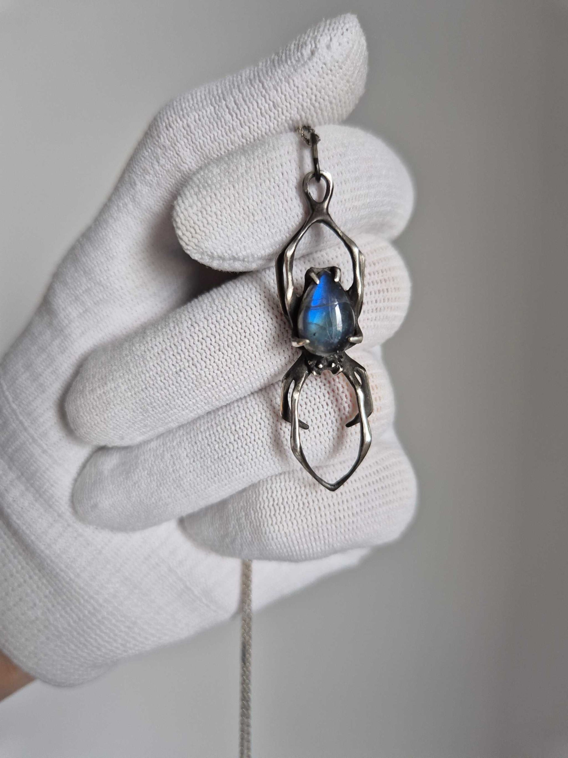 Handmade silver Spider necklace with blue labradorite, held in a gloved hand for scale and detail.