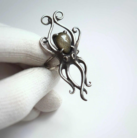 Tactile silver Octopus ring held in white glove, showing intricate tentacle details and gemstone