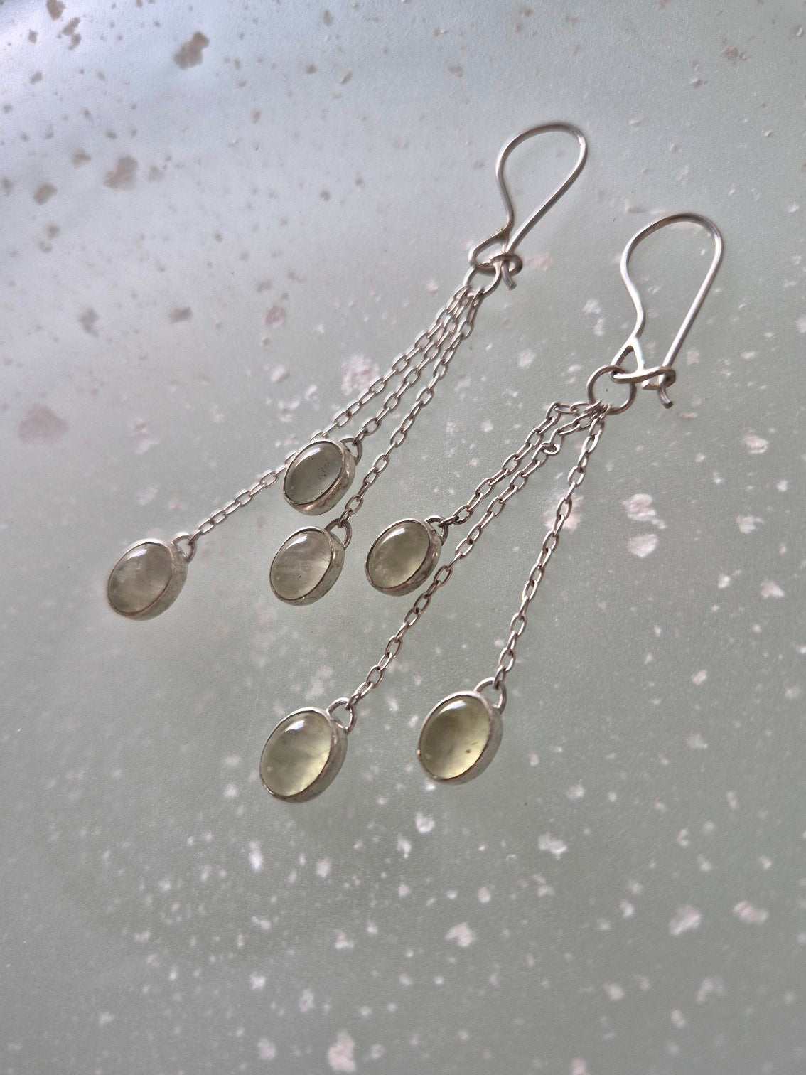 Delicate green dangle earrings with prehnite gemstones shown on soft neutral backdrop