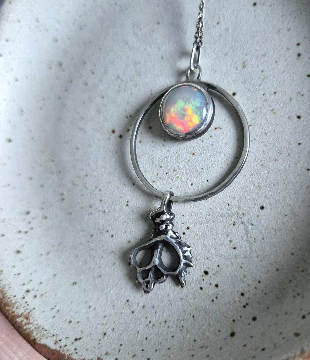 Close-up of silver opal necklace with a seashell-shaped charm, resting on light background