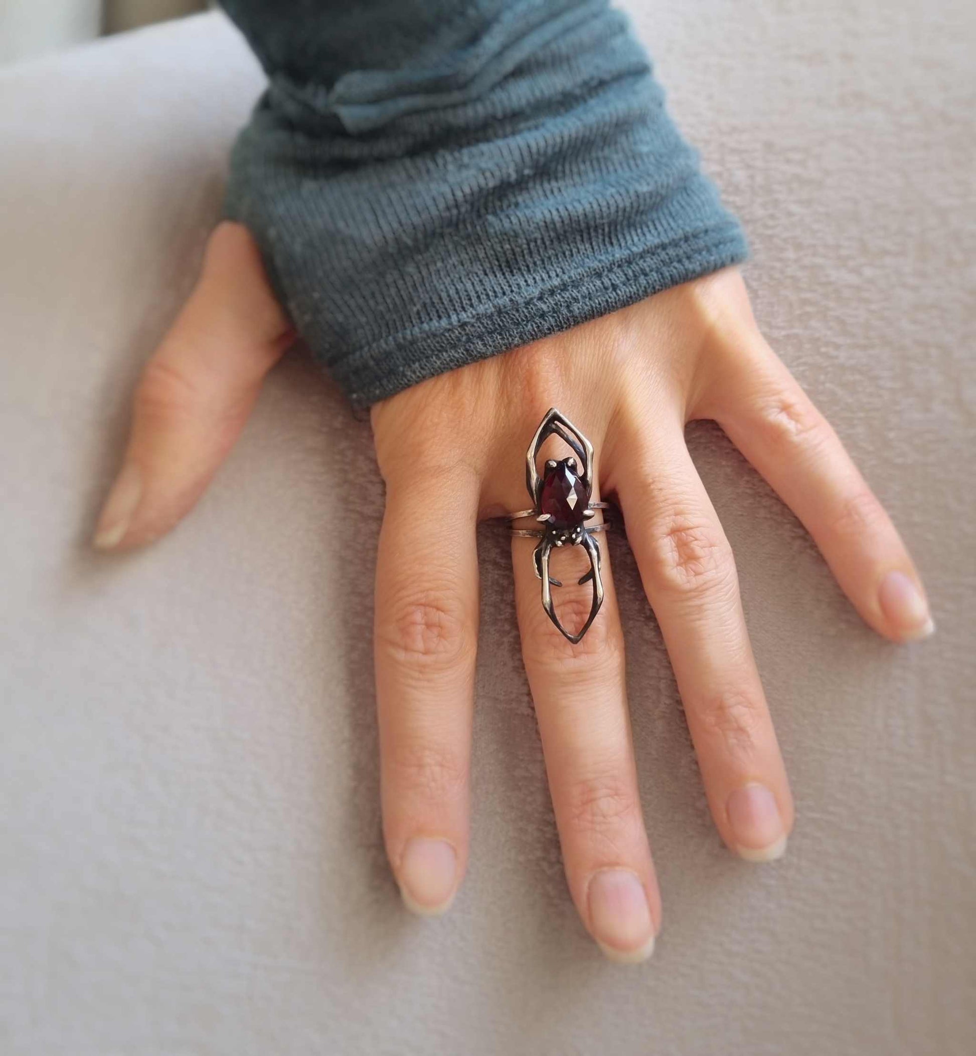Front view of silver Spider ring worn on gloved hand, with symmetrical openwork frame and deep red gemstone