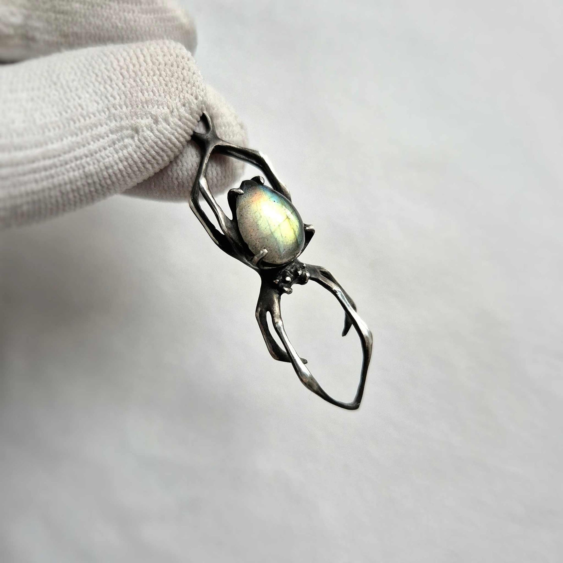 Handcrafted Spider pendant with labradorite resting on light stone