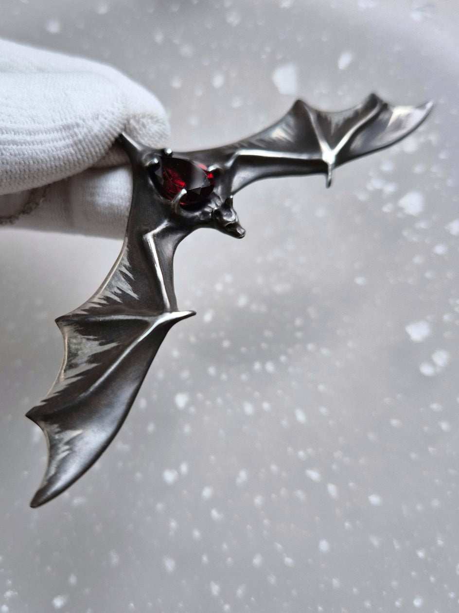 Wide-winged Silver Bat necklace with a faceted natural garnet gemstone, captured from an angle.