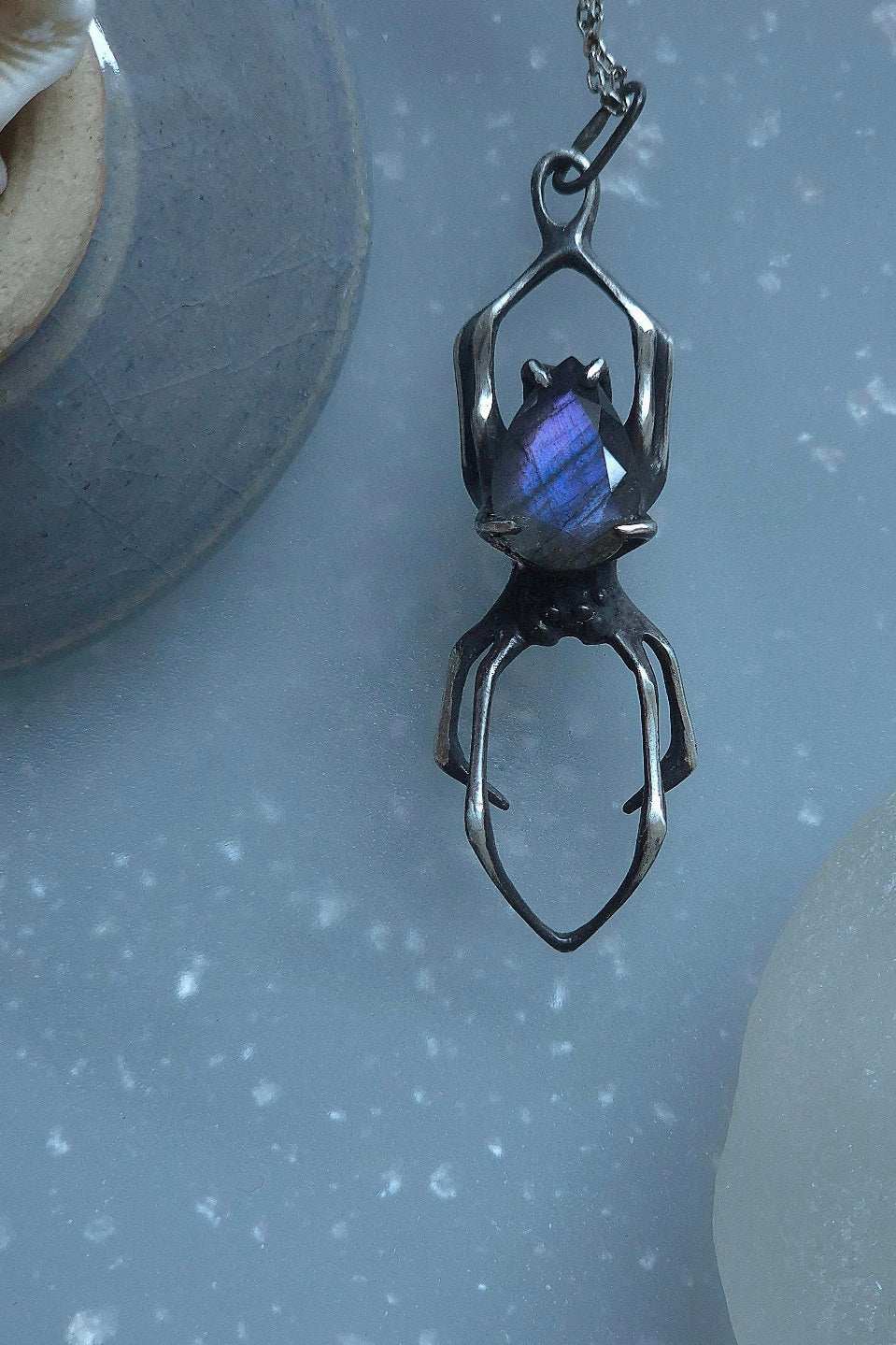 Detailed shot of silver Spider necklace with a purple labradorite gem, positioned under soft natural light