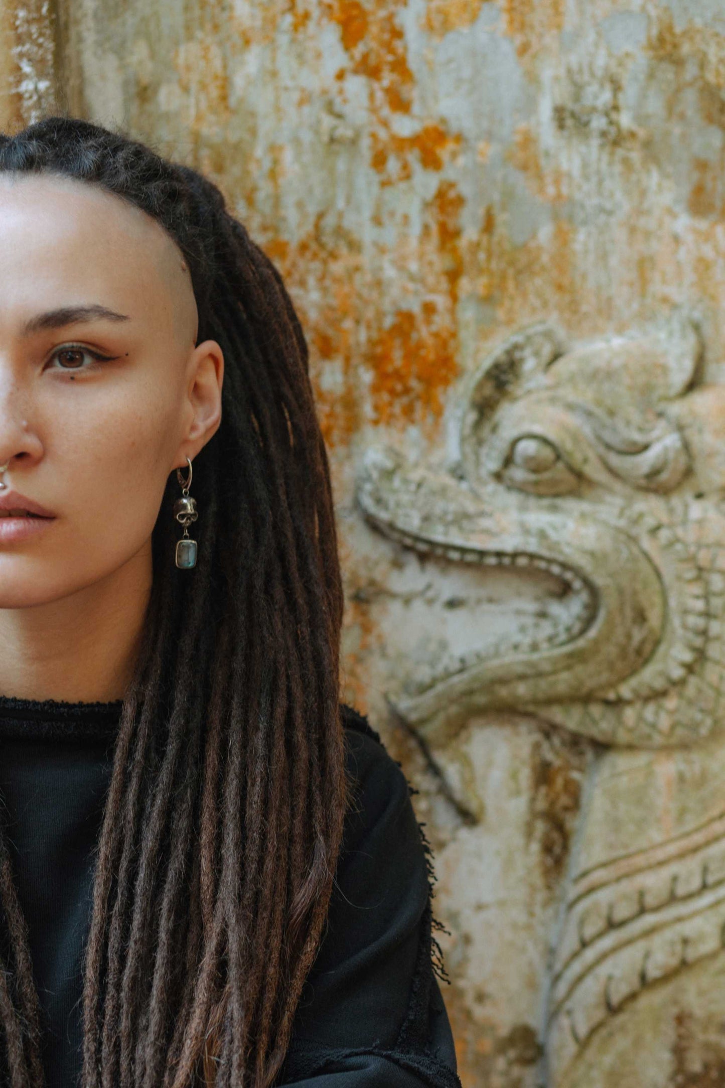 Silver Skull earrings with labradorite gemstones, worn by a model with dreadlocks, against an ancient wall with ethnic vibe