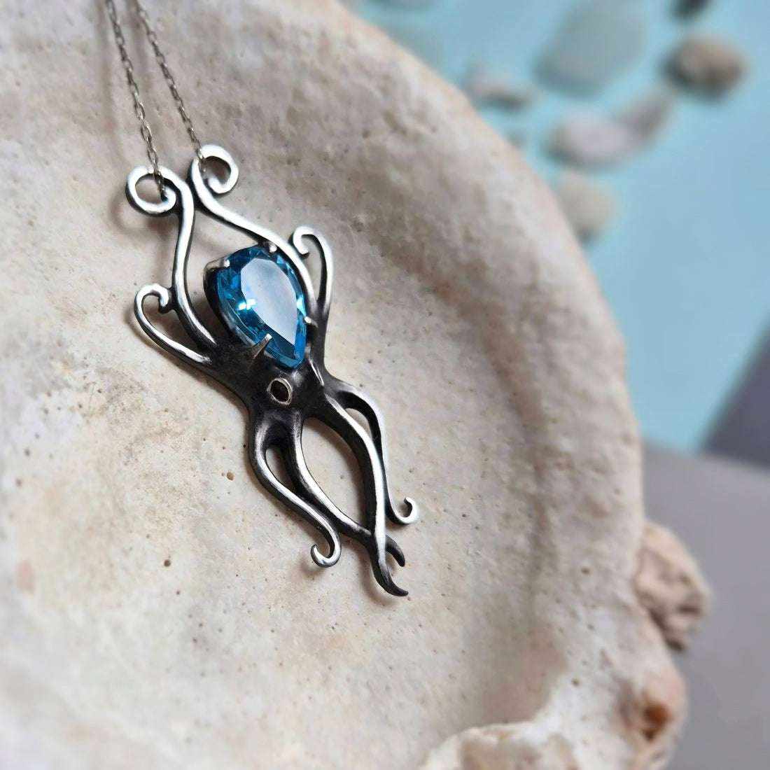 Close-up of silver Octopus necklace with vivid blue gemstone, placed in a textured seashele-up of silver Octopus necklace with vivid blue gemstone, placed in a textured seashell