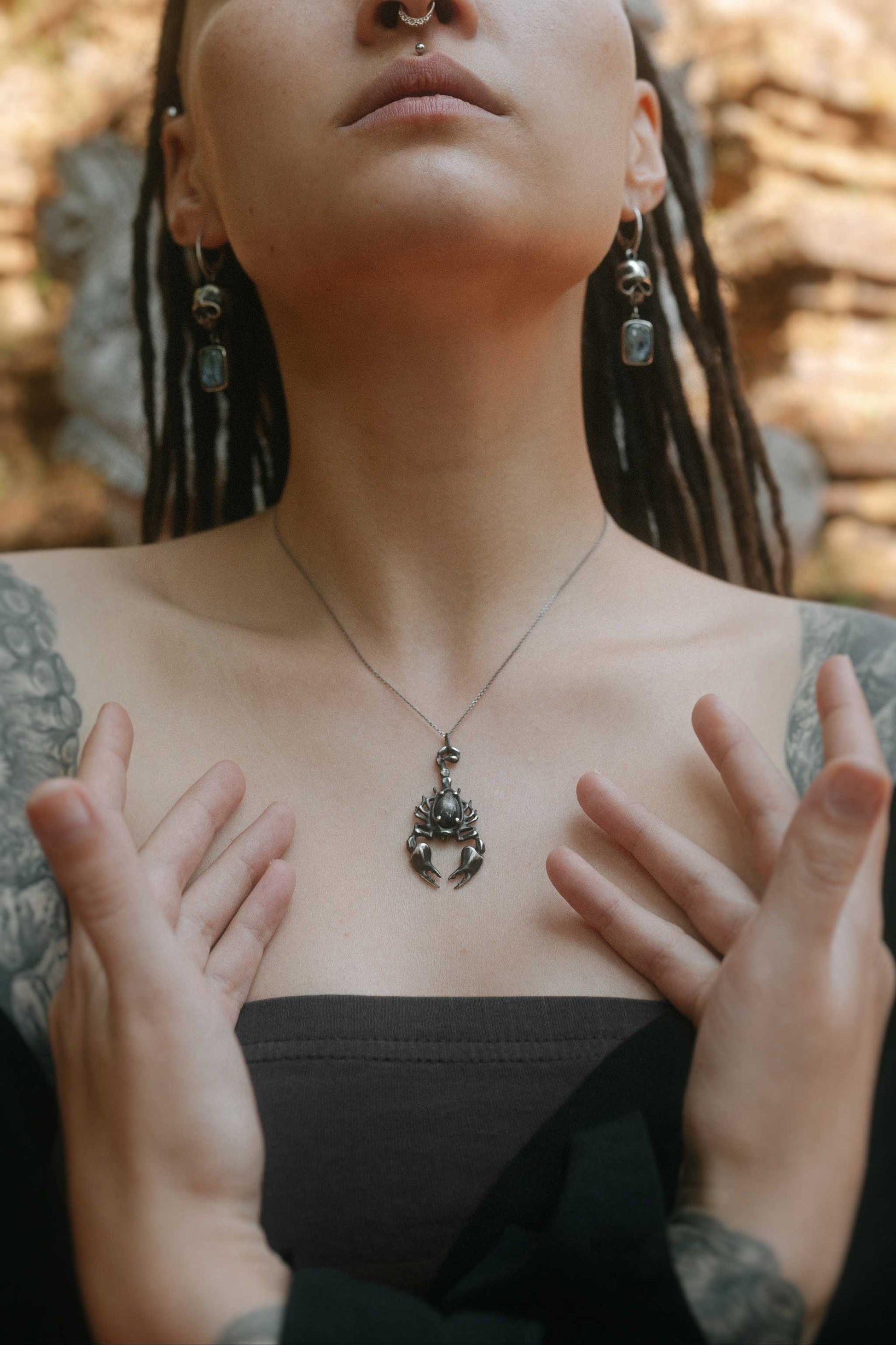 model in black off-shoulder top wearing the silver Scorpion necklace, with textured background and shaman vibe