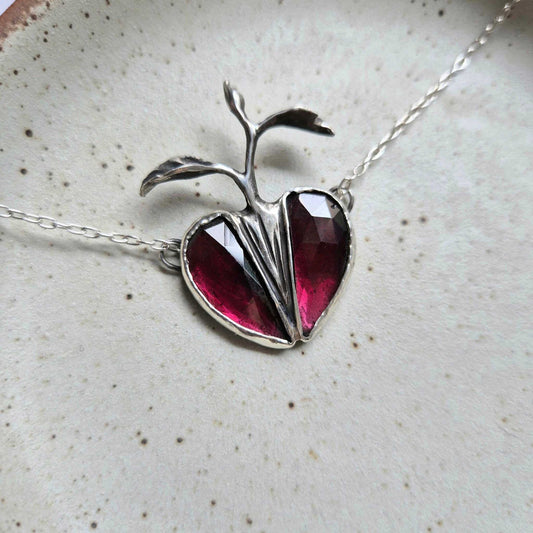 Close-up of silver Seed Heart necklace with rosecut garnets forming a heart shape, displayed on a white ceramic surface.