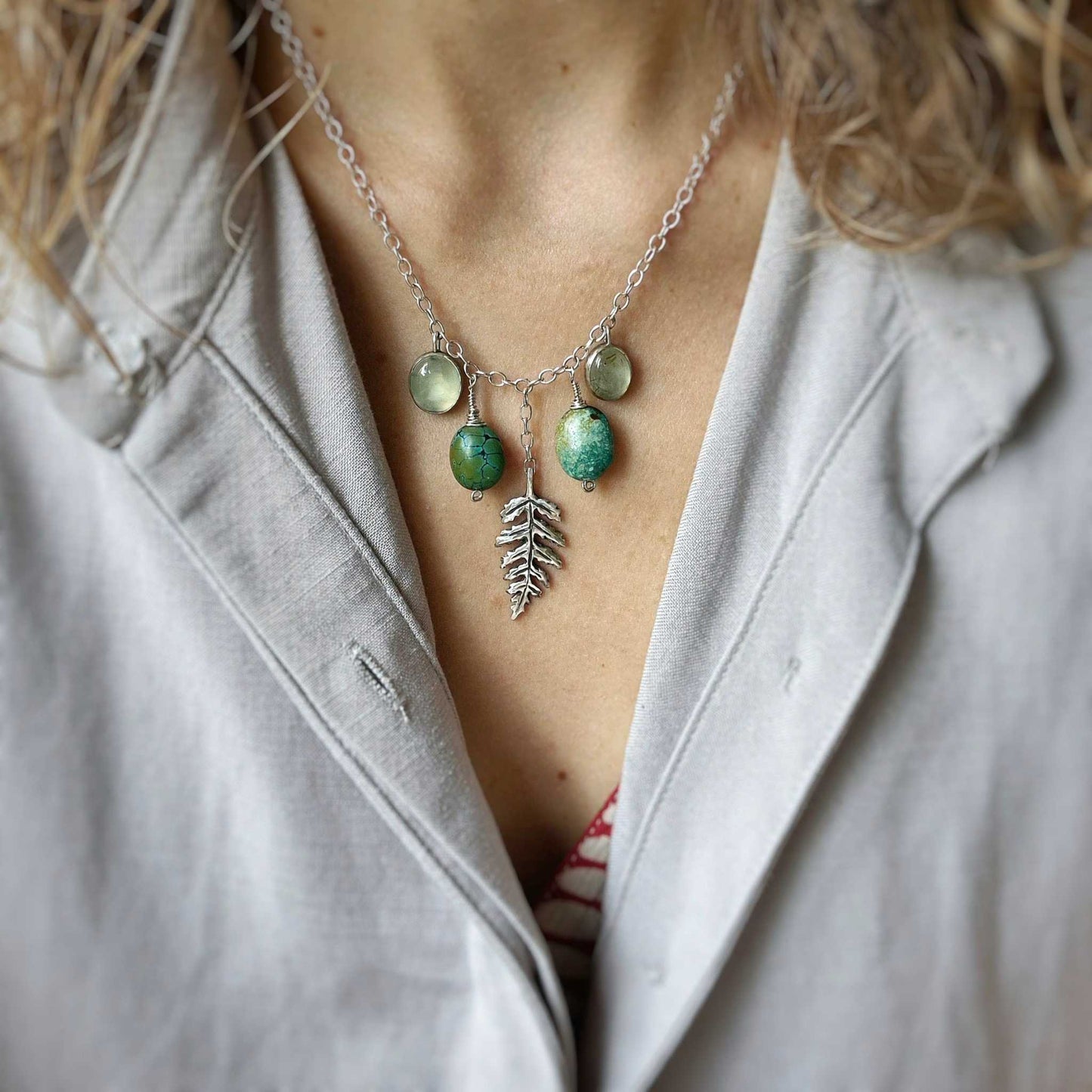 urquoise and prehnite gemstone necklace with silver leaf pendant, worn on the neck over a soft grey blouse.