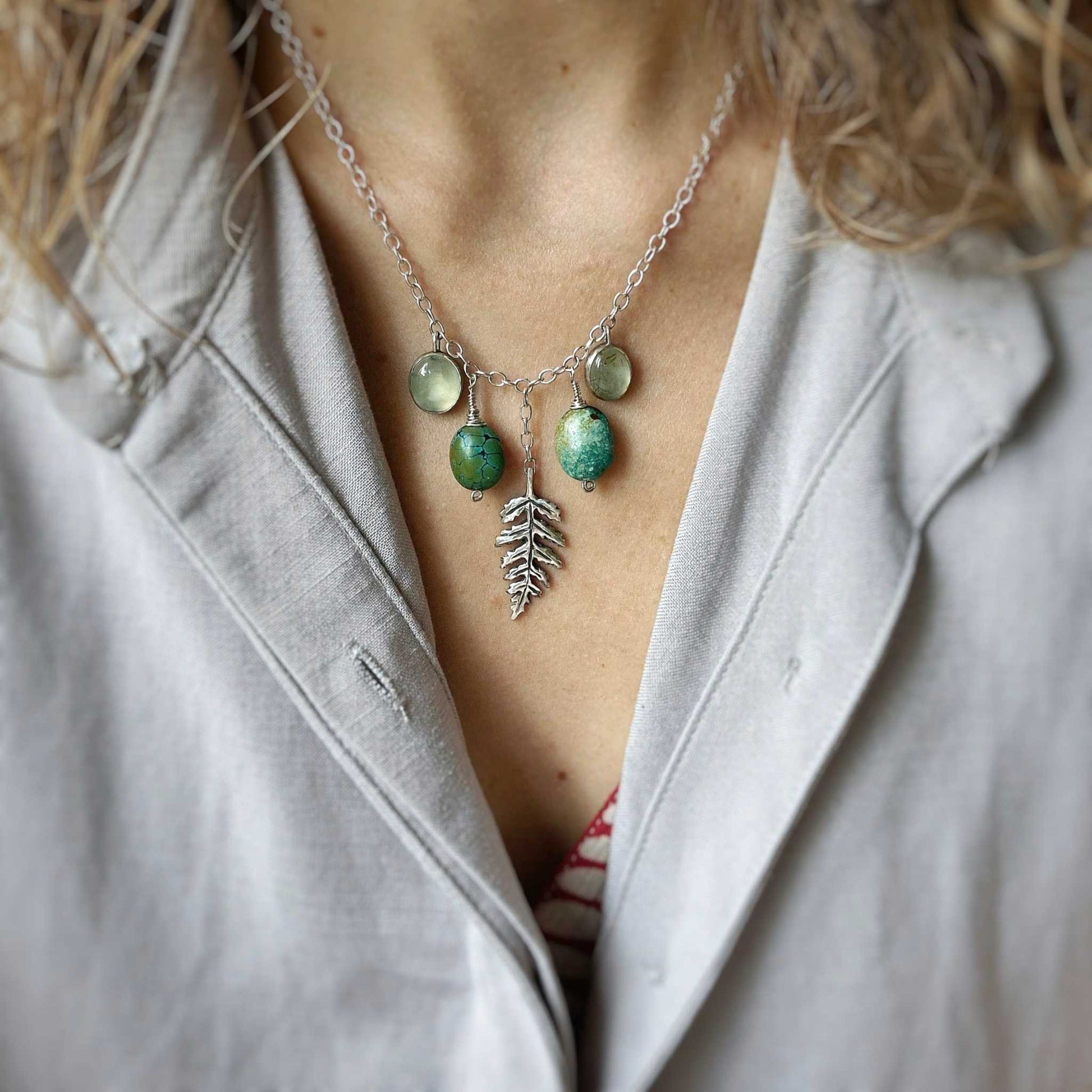urquoise and prehnite gemstone necklace with silver leaf pendant, worn on the neck over a soft grey blouse.