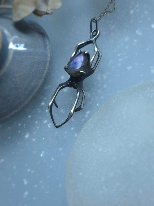 Oxidized silver Spider pendant with teardrop-shaped purple labradorite, styled beside natural objects