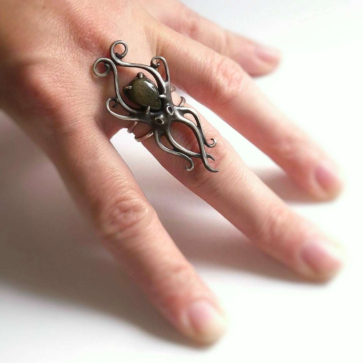 Close-up of handmade octopus-shaped silver ring on finger, with elegant curved tentacles