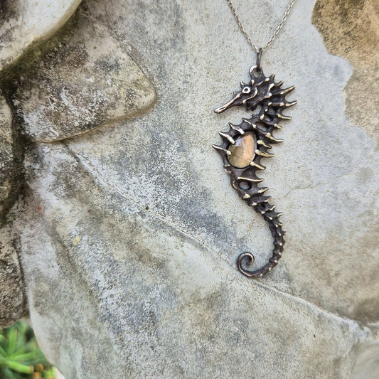 Sculptural silver Seahorse necklace with labradorite center, resting on a beach rock