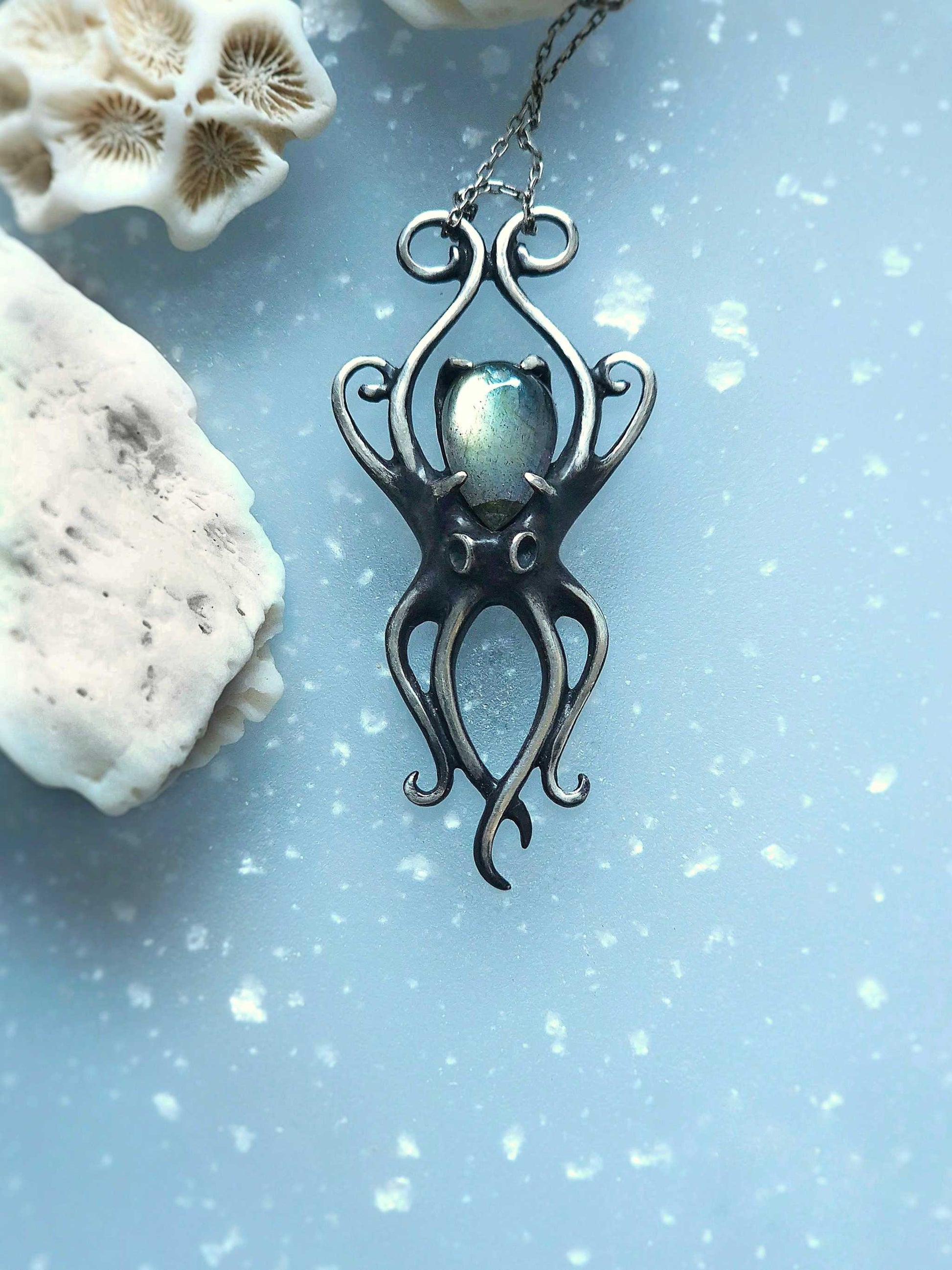 Handcrafted silver octopus necklace with labradorite, displayed on blue textured background with coral