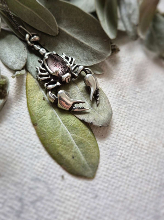 Side view of the handmade Scorpion pendant resting on a leaf, showing detailed legs and tail.