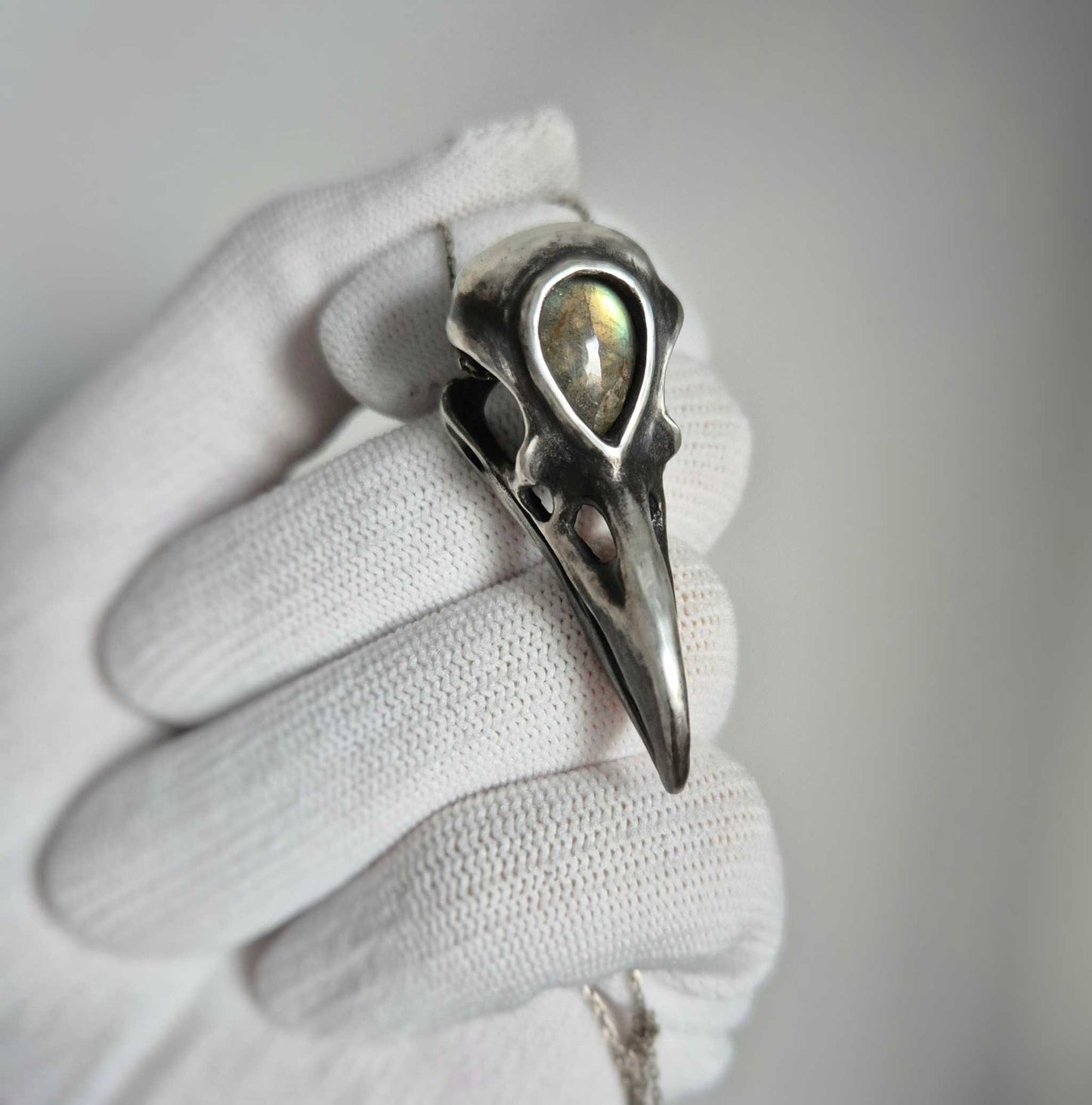 Oxidized silver raven skull pendant with labradorite, on white glove background