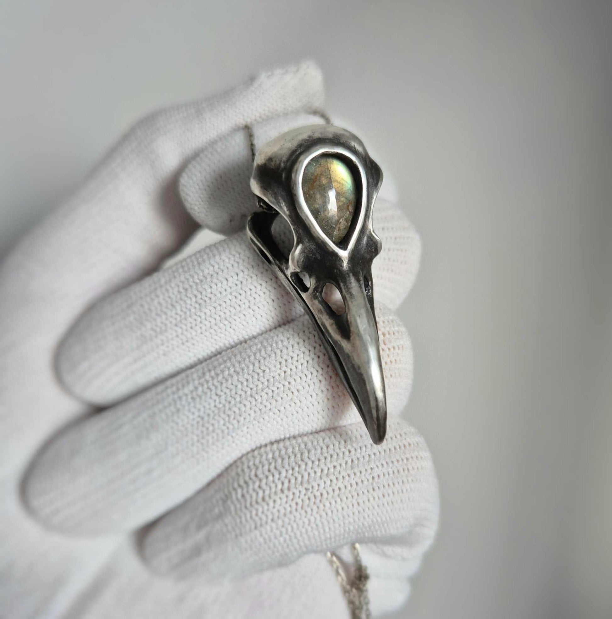 Oxidized silver raven skull pendant with labradorite, on white glove background