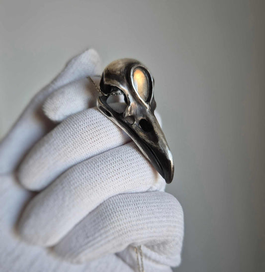 Silver raven skull necklace with golden labradorite, held in gloved hand for close-up detail.
