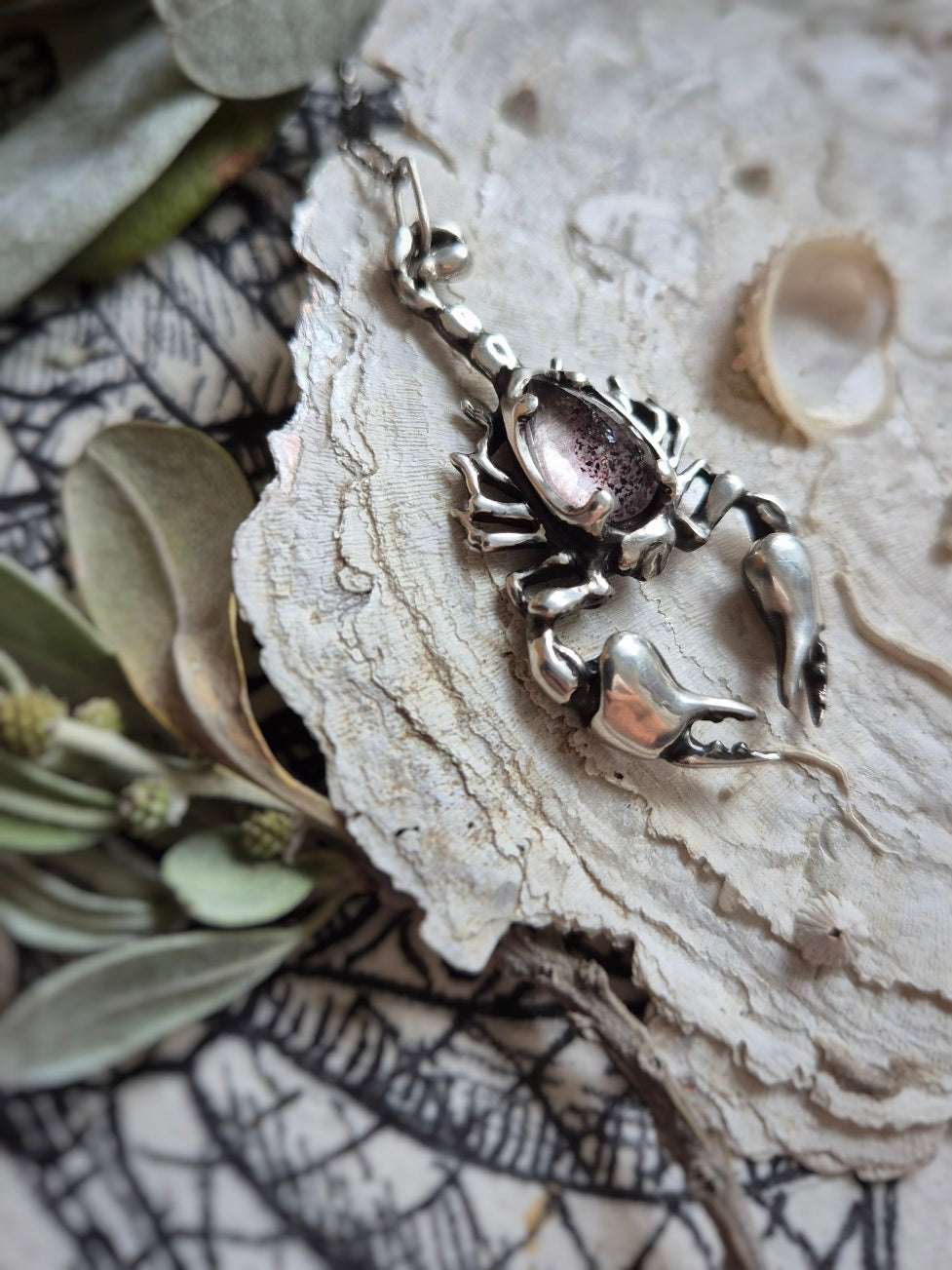 Silver Scorpion necklace displayed on natural background with shells and netting, highlighting the gemstone.