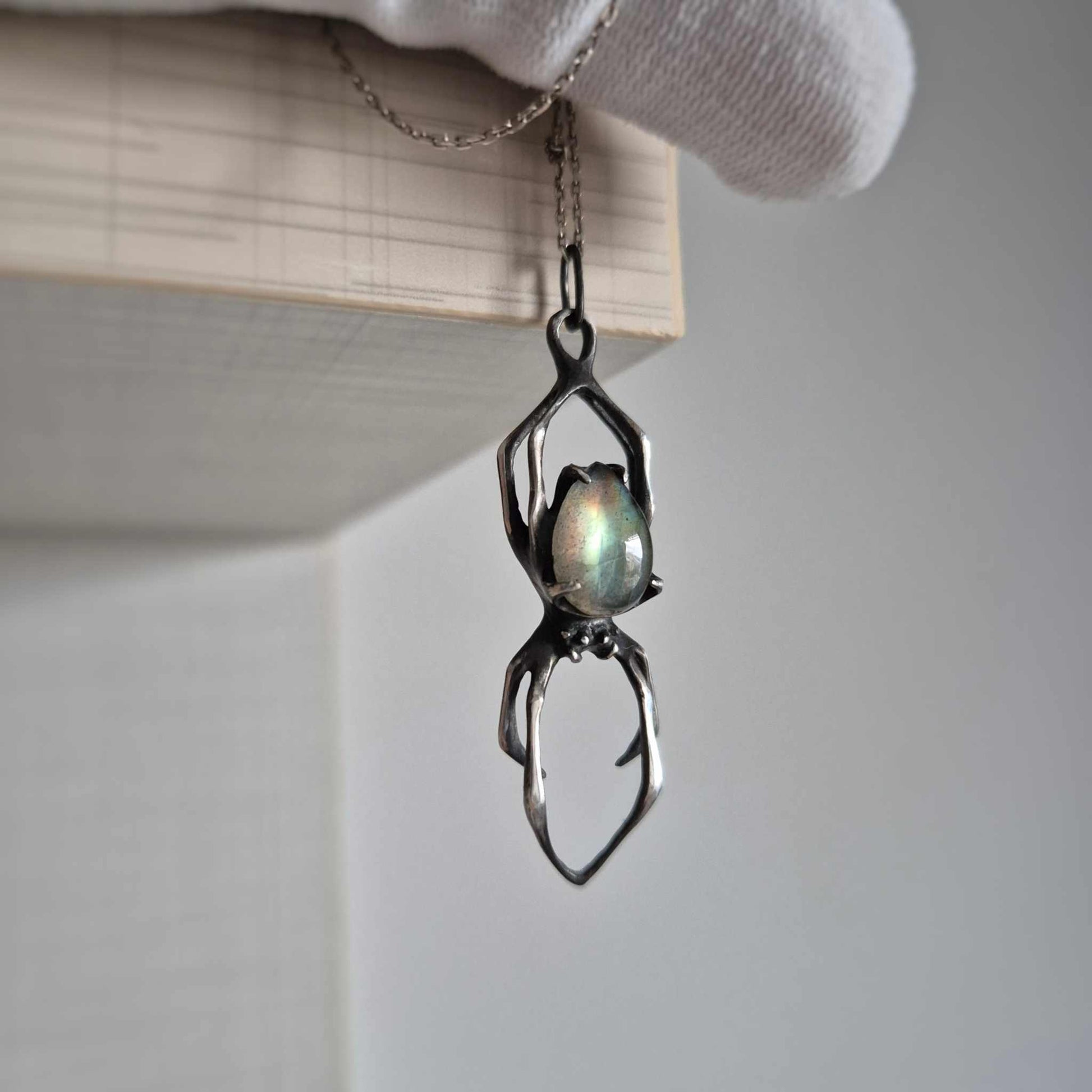 Silver Spider necklace with oval labradorite, captured mid-hanging