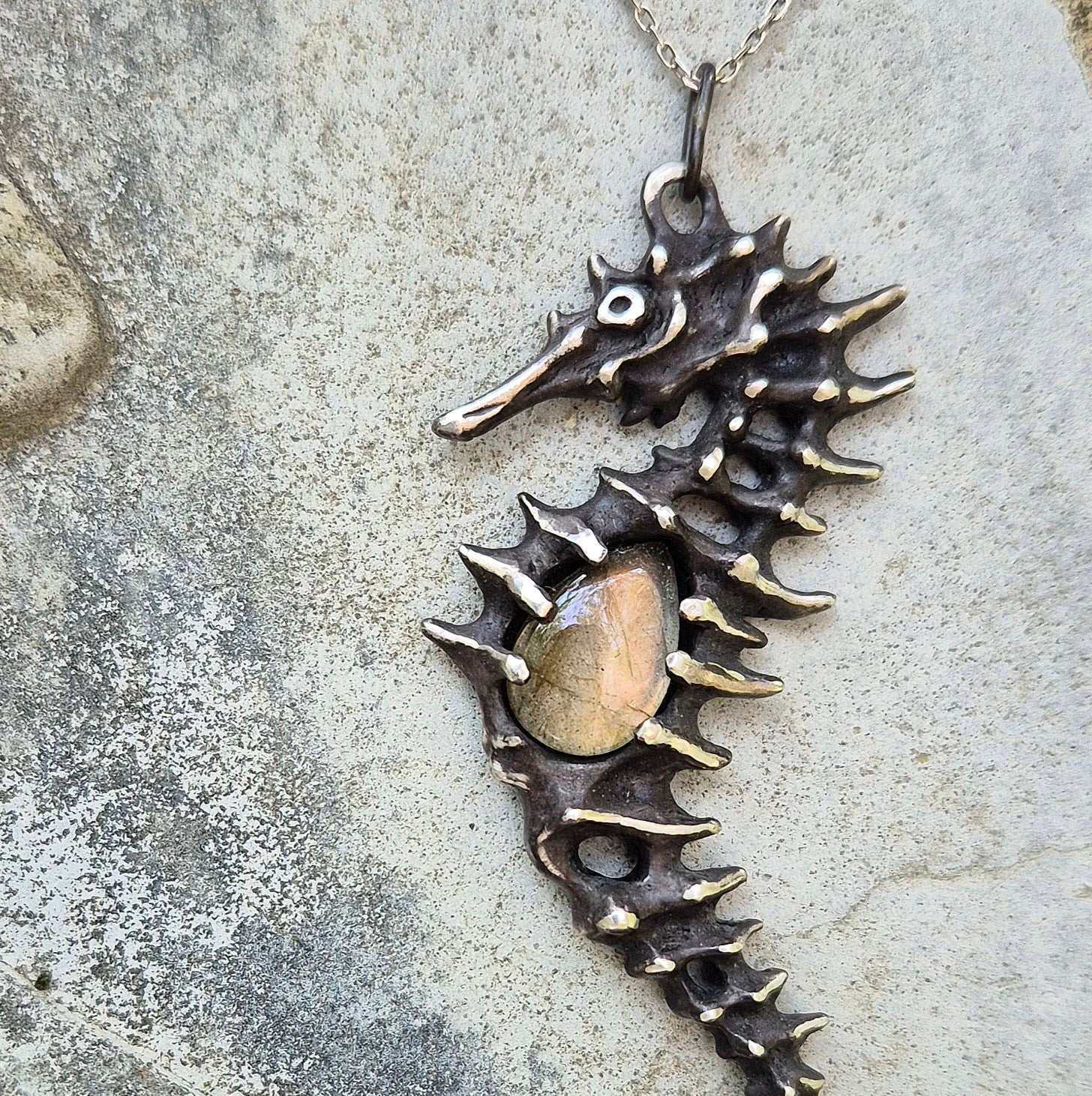 Close-up of a silver Seahorse necklace with sculpted texture and yellow labradorite on textured stone background