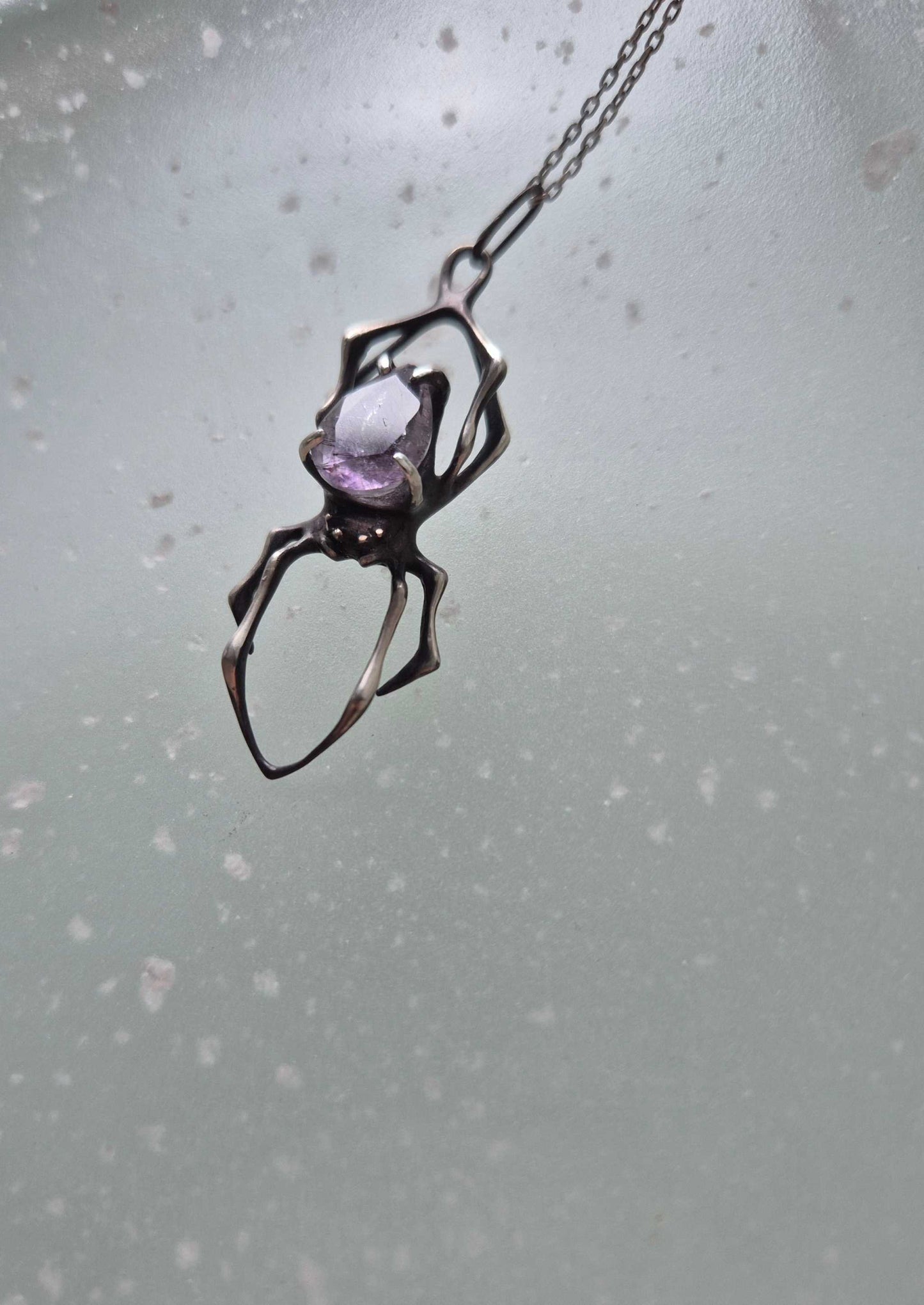 Silver spider necklace with super seven gemstone photographed from a distance, suspended on a chain against a foggy background