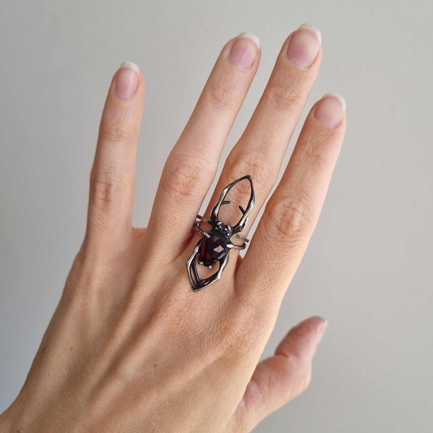 Silver Spider ring in natural light on woman's hand, capturing the contrast of oxidized silver and glowing garnet