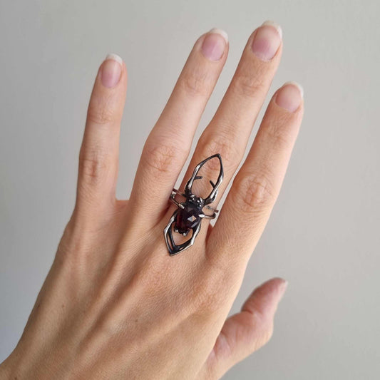 Silver Spider ring in natural light on woman's hand, capturing the contrast of oxidized silver and glowing garnet