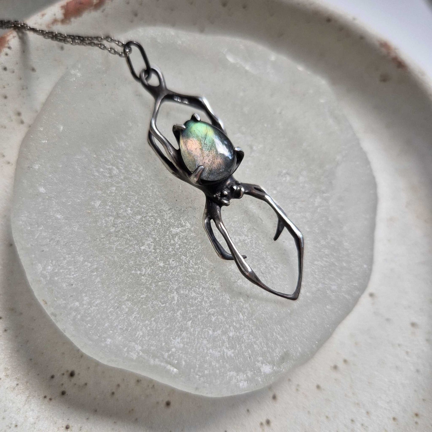 Textured silver Spider necklace with labradorite cabochon displayed on a stone disc
