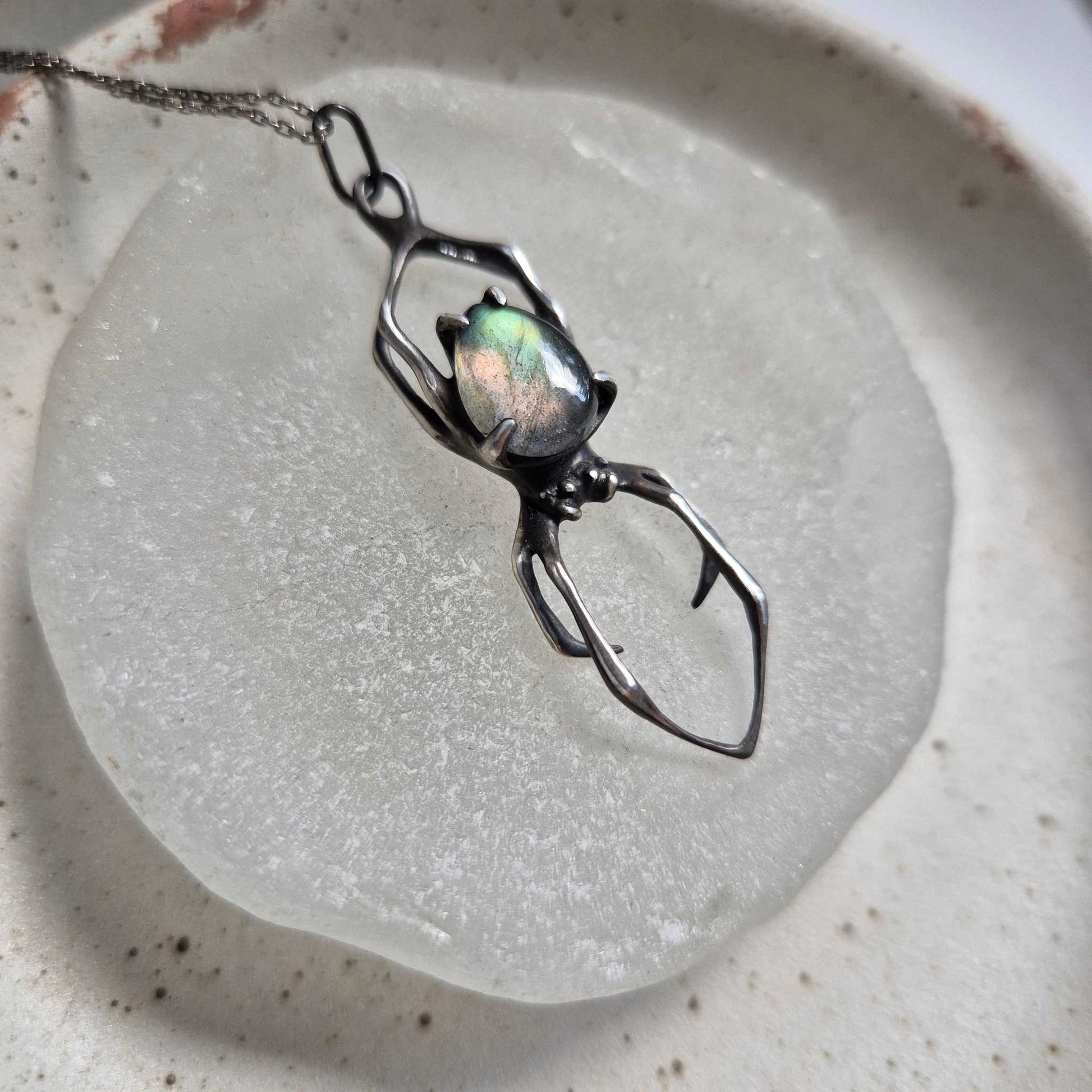 Textured silver Spider necklace with labradorite cabochon displayed on a stone disc