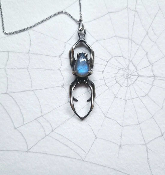 Silver Spider necklace with blue labradorite placed on a paper with spiderweb sketch background, highlighting its organic design.