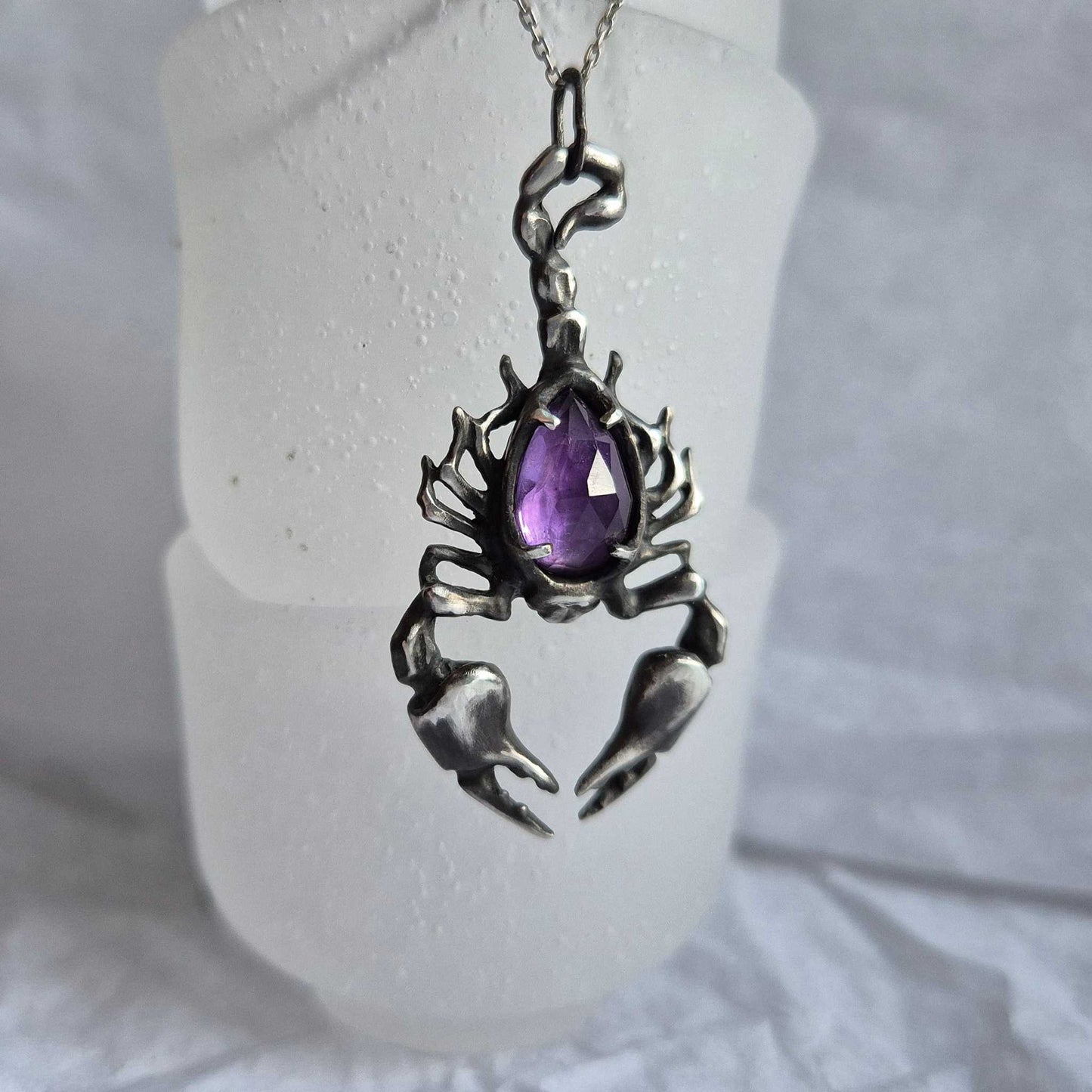 Close-up of a sculptural silver Scorpion necklace on whte glass background