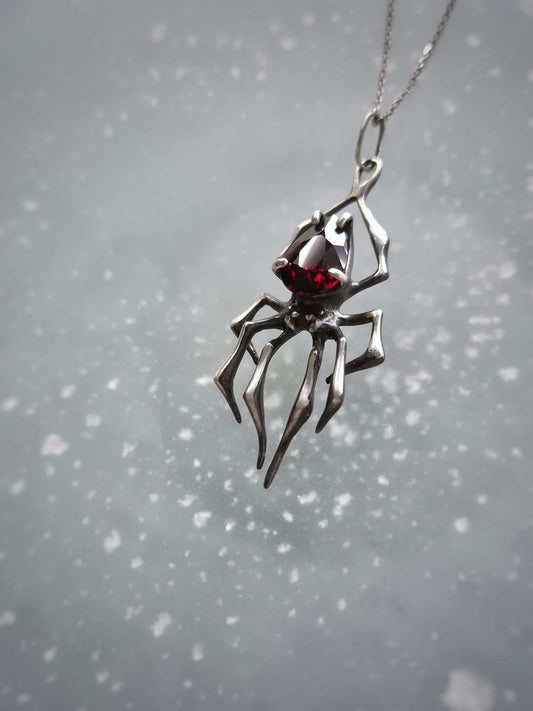 Angled view of artisan spider necklace in silver with glowing garnet gem