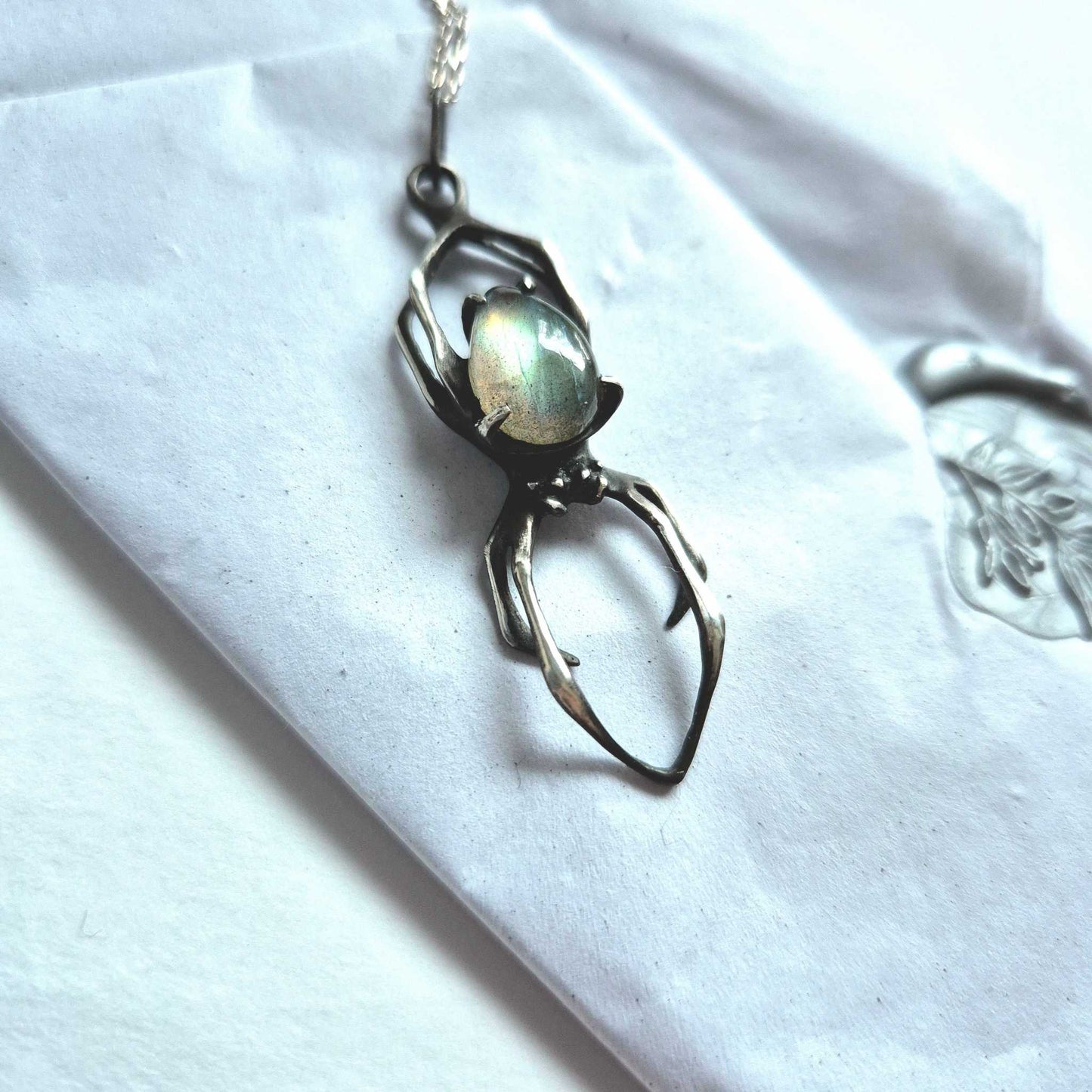 Glimmering labradorite Spider necklace on glossy ceramic surface