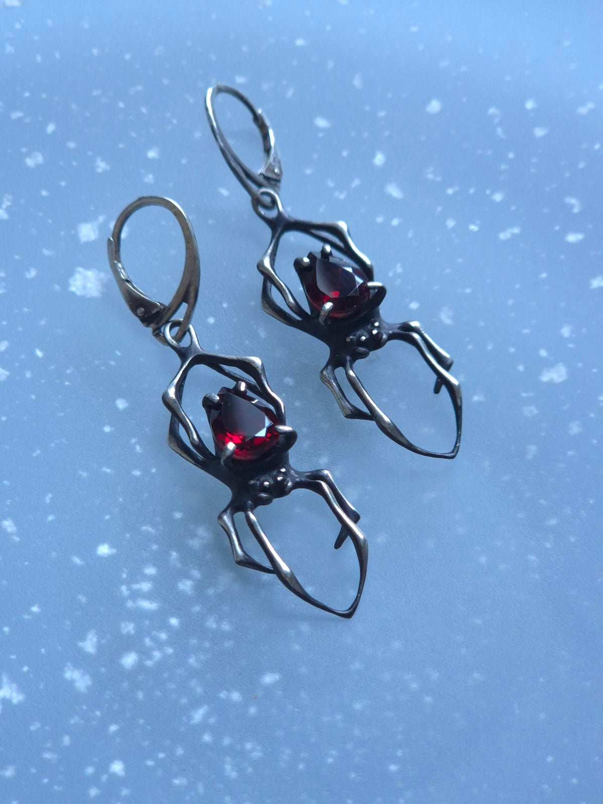 Detailed view of silver spider earrings with deep red garnets, handcrafted in oxidised sterling silver