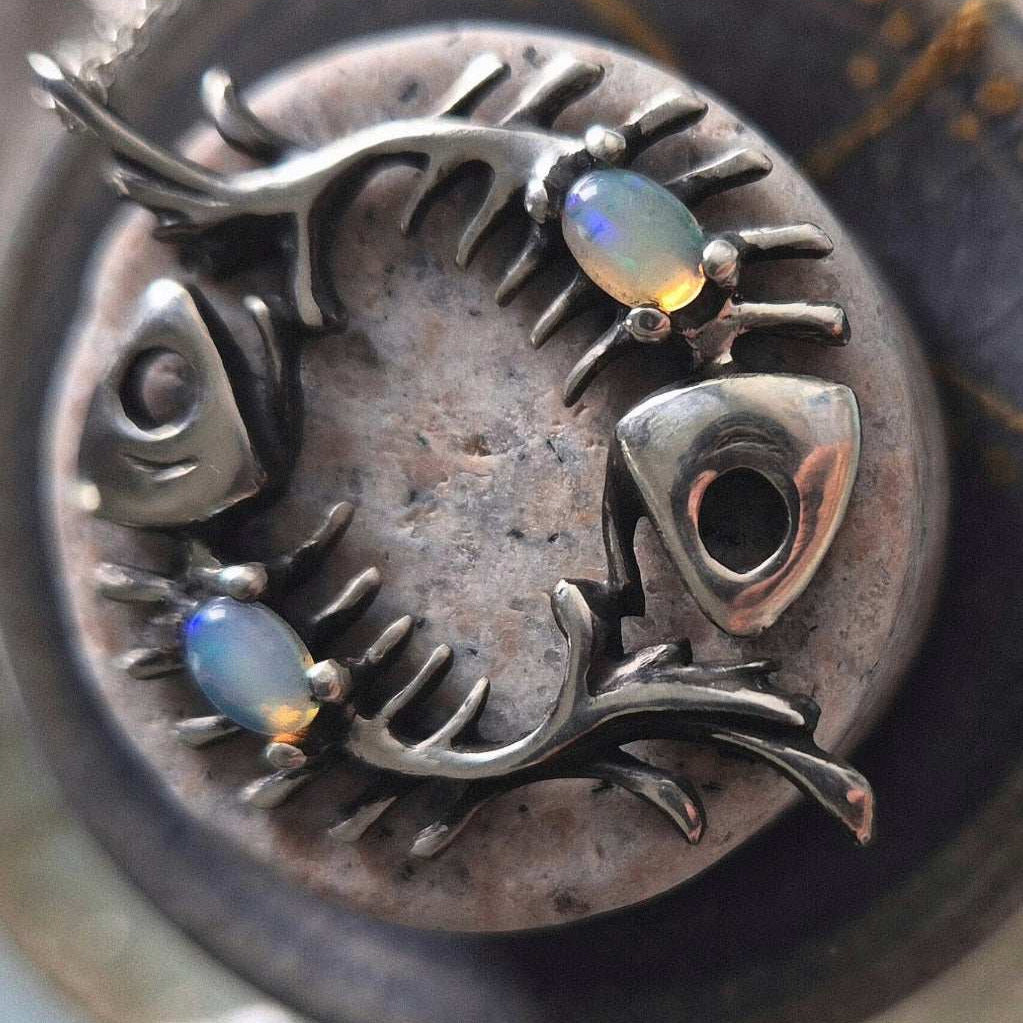 Silver fish necklace with opal gems styled on textured stone backdrop