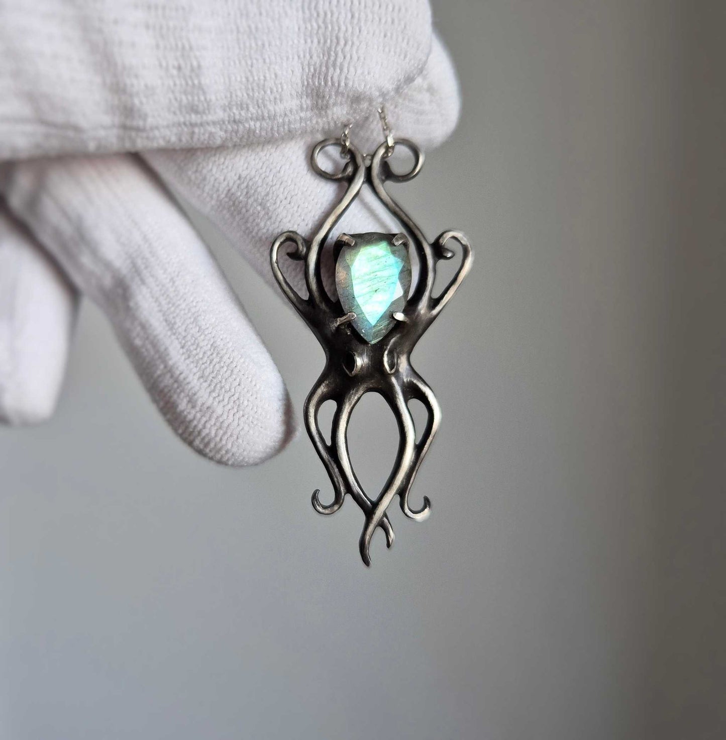 Silver Octopus necklace held in a gloved hand, showing the faceted cyan labradorite