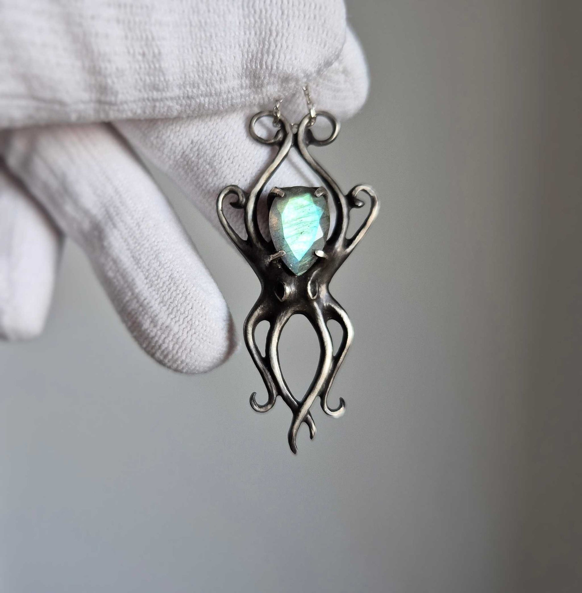 Silver Octopus necklace held in a gloved hand, showing the faceted cyan labradorite