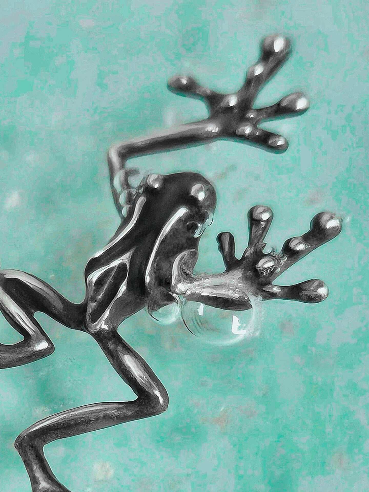Close-up of a sculpted sterling silver frog pendant, showing its raised forelegs and webbed toes on aqua