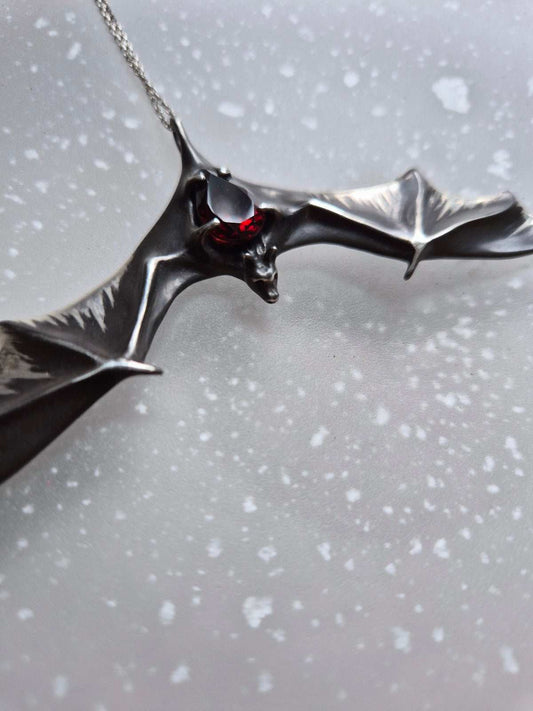 Cllose-up of Silver Bat necklace featuring a natural garnet gemstonever Bat necklace lying on a translucent textured background