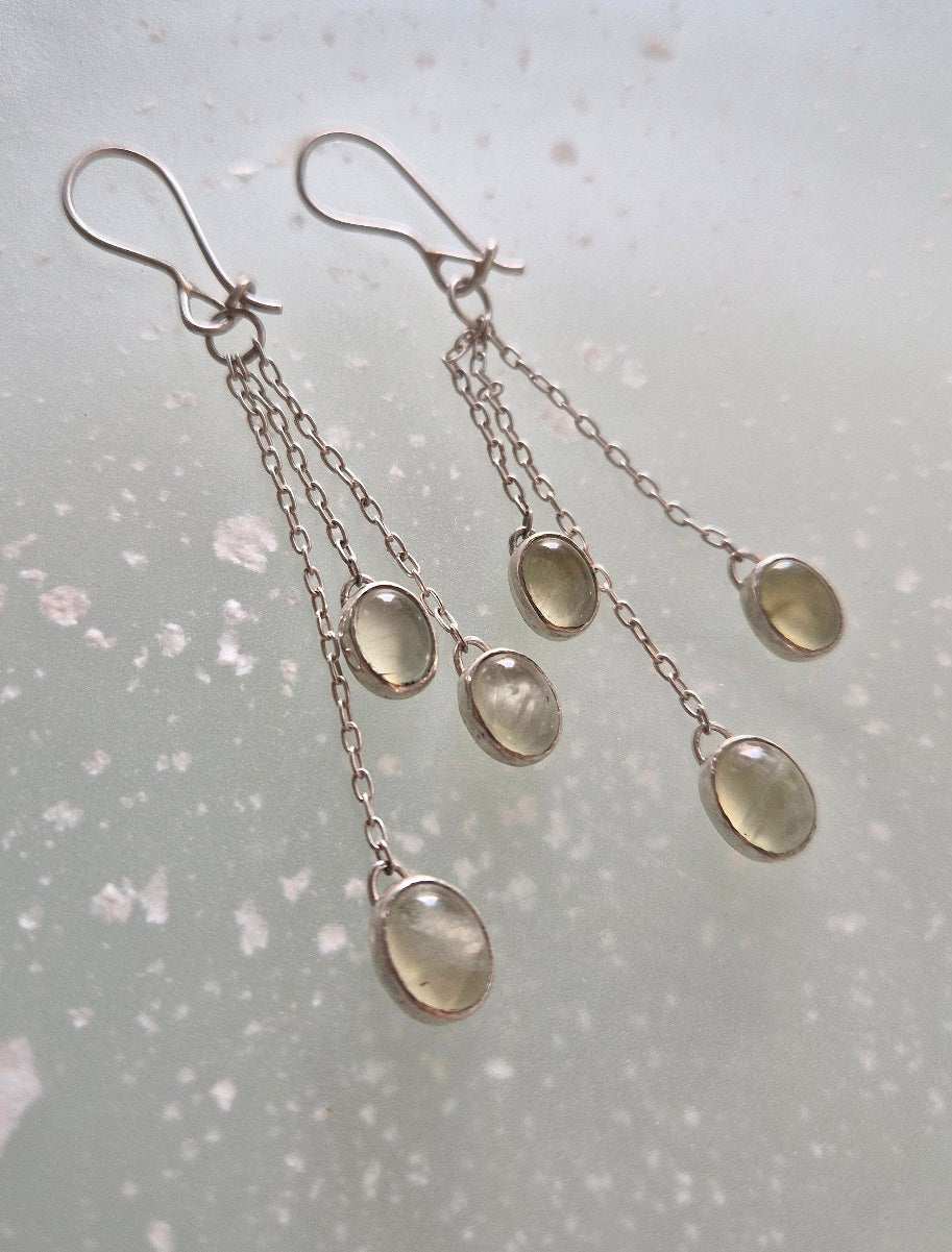 Natural prehnite green dangle earrings with silver hooks on textured neutral surface