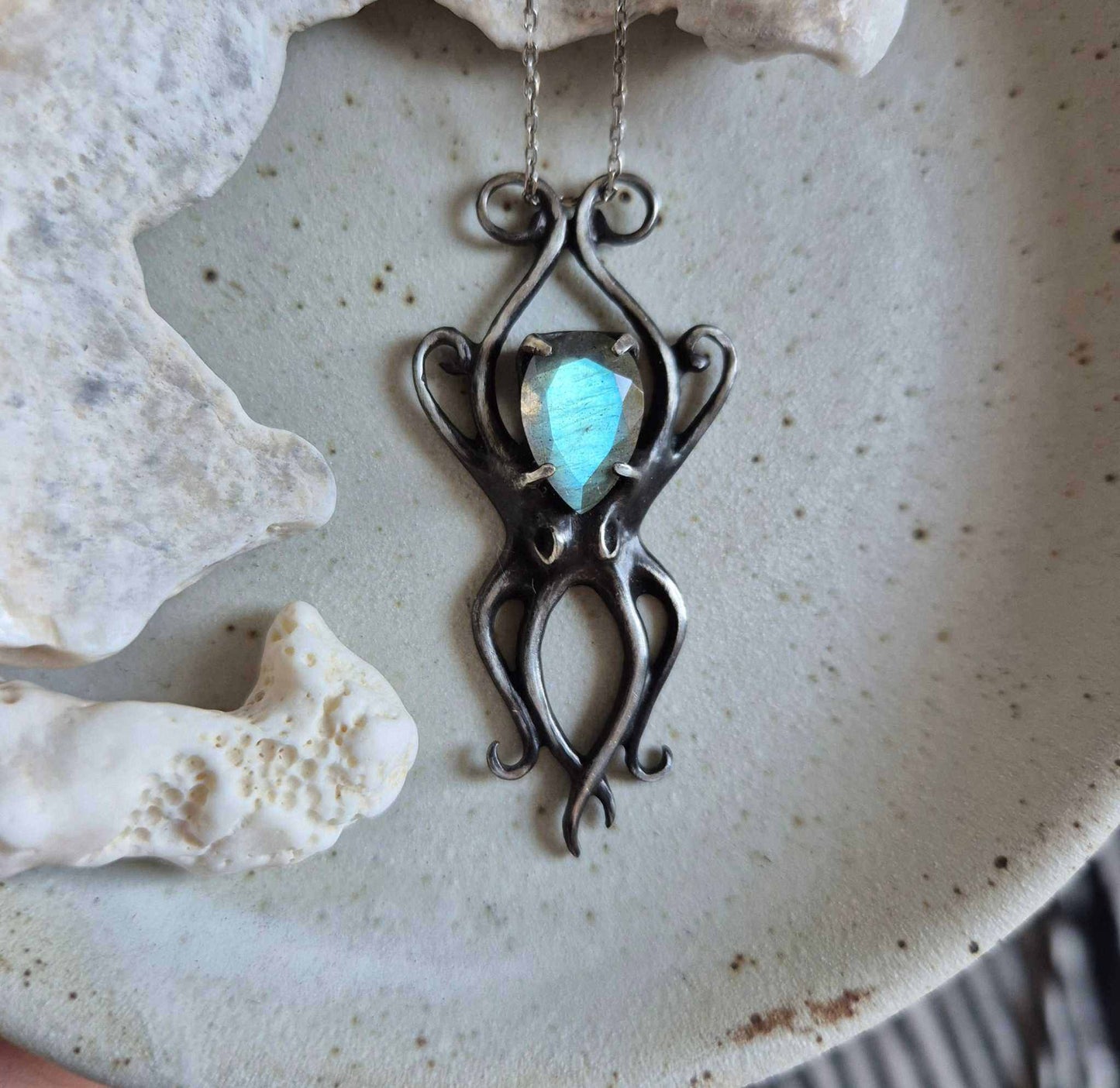 Close-up of silver Octopus pendant with cyan labradorite on ceramic background with corals